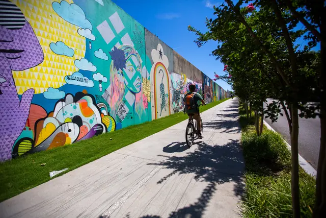person riding bike on sidewalk beside a wall with a colorful mural
