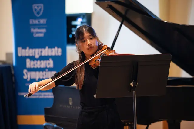 Yujin Ha, a young female student, plays a violin in front of a banner that says Undergraduate Research Symposium