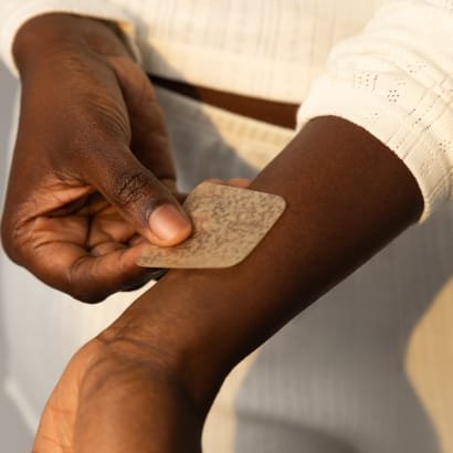 An arm extends while a hand applies a patch to a wrist.