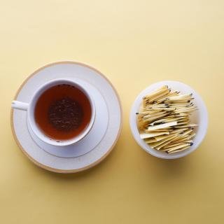 An overhead image of a spoon, teacup on saucer, and cup of yellow artificial sweetener packets against a yellow backdrop