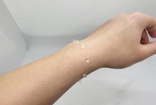 A thin threaded bracelet with beads worn on a person’s wrist
