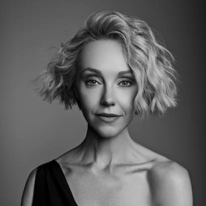 A woman with short blonde hair, wearing a low cut black dress.
