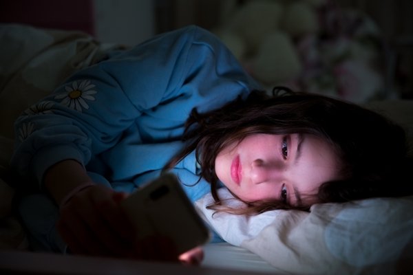 young girl laying in bed looking at phone screen