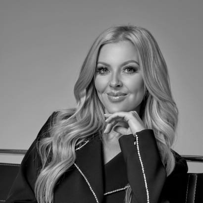 A blonde woman in a black jacket props her chin on her hand.