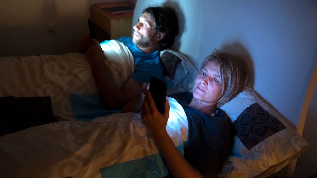 Couple checks a phone while in bed before sleep.
