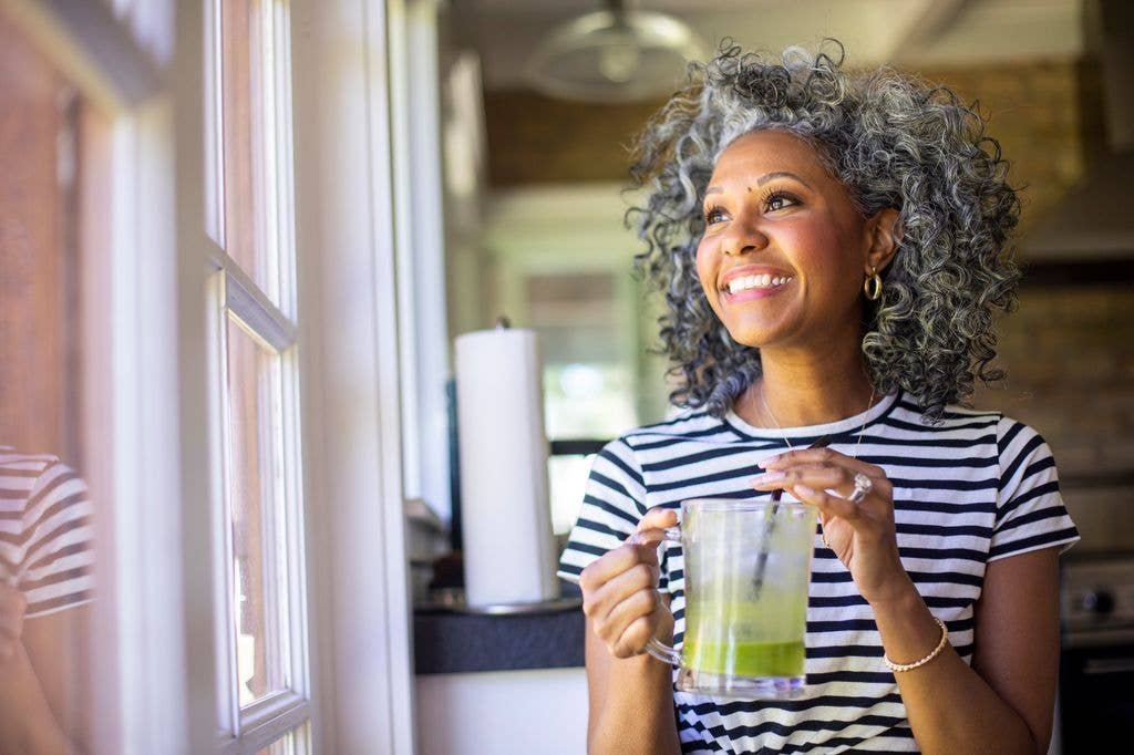 A beautiful black woman with white curly hair drinks coffee in her kitchen