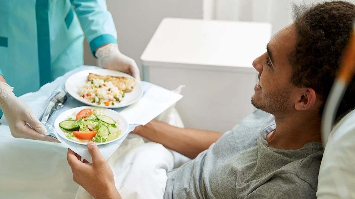 A man receives a tray of food from a nurse in a hospital.