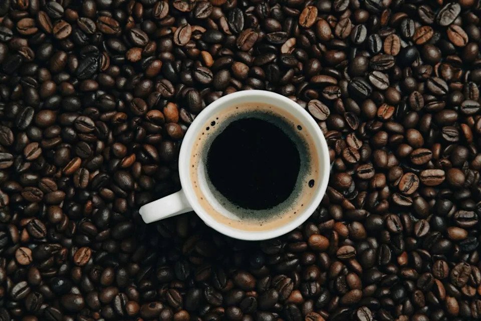 a cup of coffee sitting on top of a pile of coffee beans