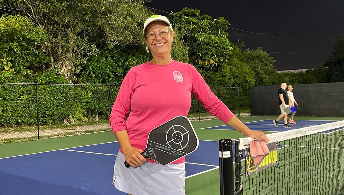 UHealth patient Odalis Pereira holding a pickleball paddle beside a net on an outdoor court at night, with other players visible in the background.