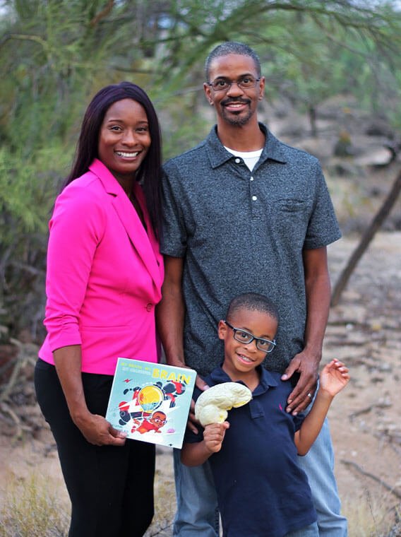 Family standing outdoors with a child holding a brain model and a brain-themed children's book.