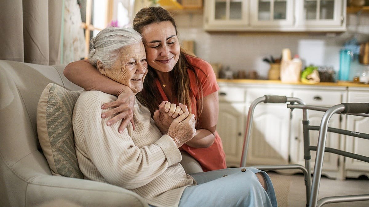 Daughter hugs senior woman with walker at home
