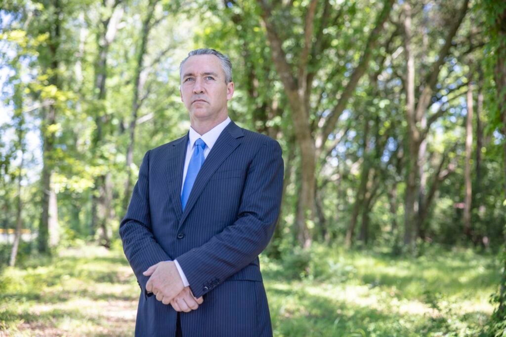 Pastor Tony Spell at Life Tabernacle Church in Baton Rouge poses for a photo wearing a suit while standing with a copse of trees in the background.