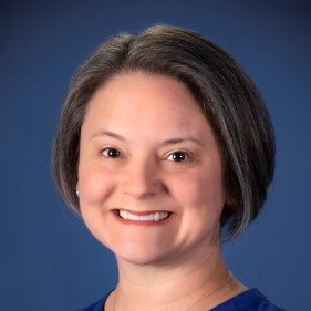 Headshot of Tara Niendam smiling, wearing a blue top, against a blue studio background.
