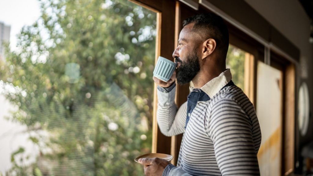 A man drinks a cup of coffee as he looks out of a window