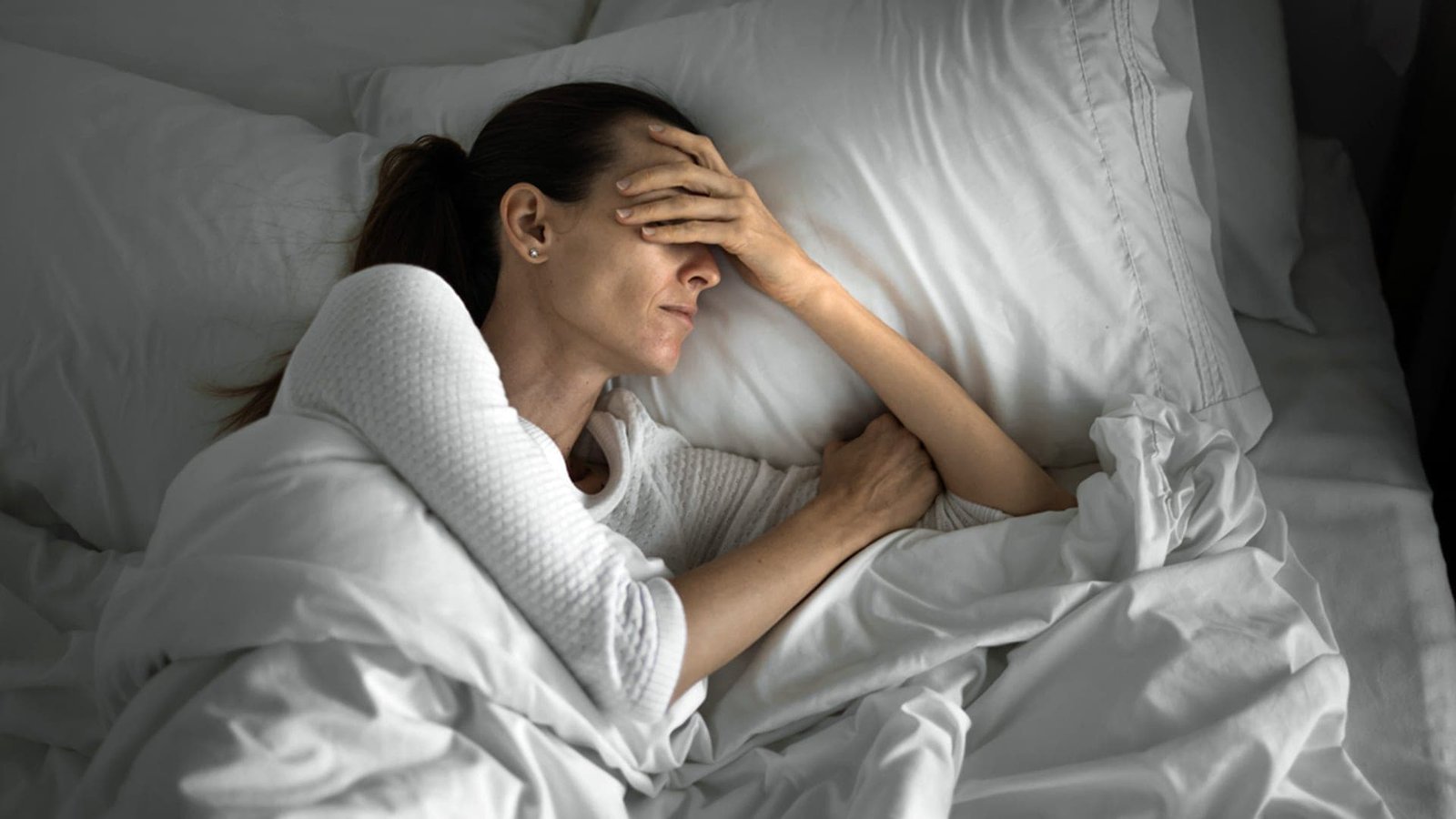 Woman lying awake in bed with her hand covering her forehead.