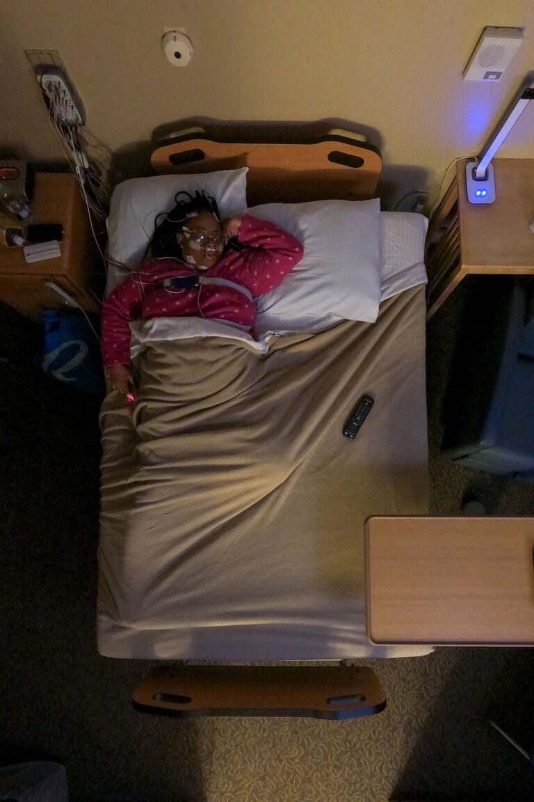 Overhead view of a patient lying in bed with subtle blue light from a television illuminating the room.