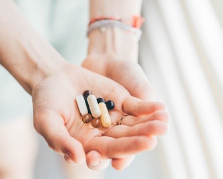 Hands holding a variety of supplement pills in various shapes, colours and sizes