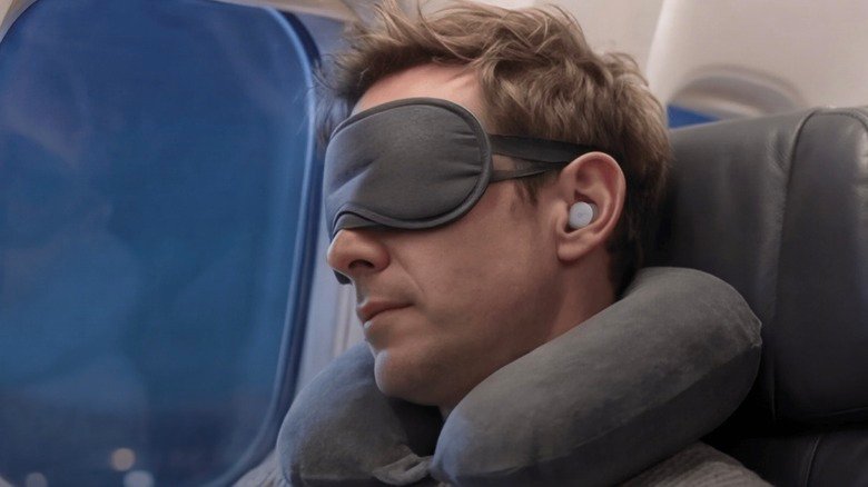 A man wearing an eye mask and Soundcore's A30 sleep earbuds during a flight.
