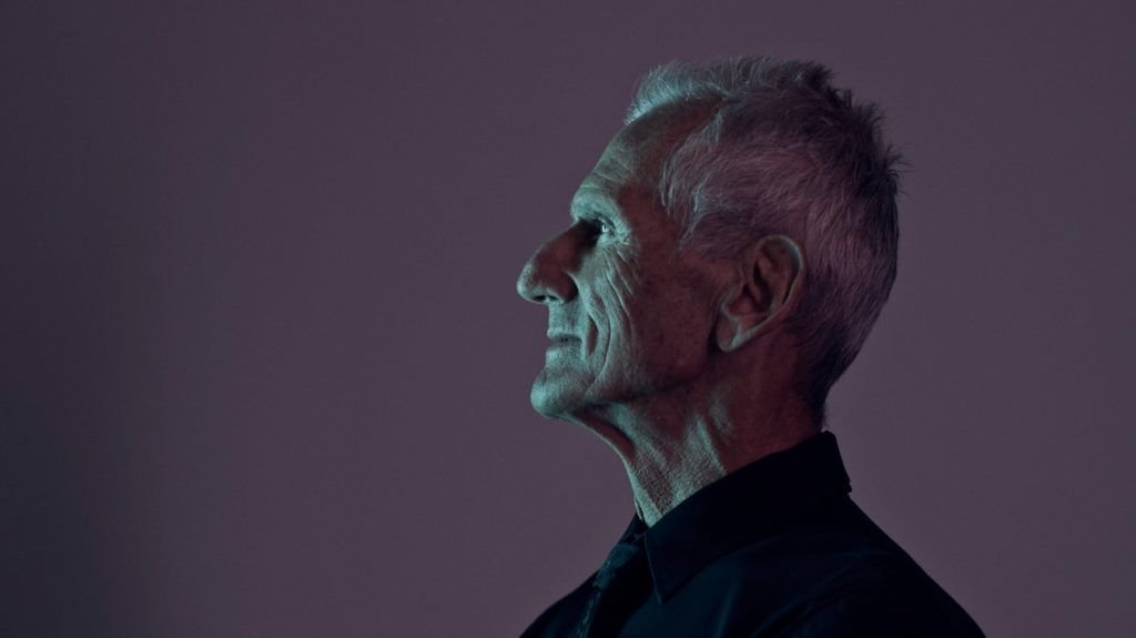 The side profile portrait of an older adult man, with coloured lights in the background
