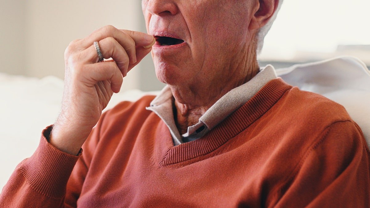 senior man puts pill into his mouth