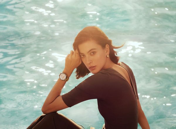 Woman relaxing by a pool and checking health data on her smartwatch.