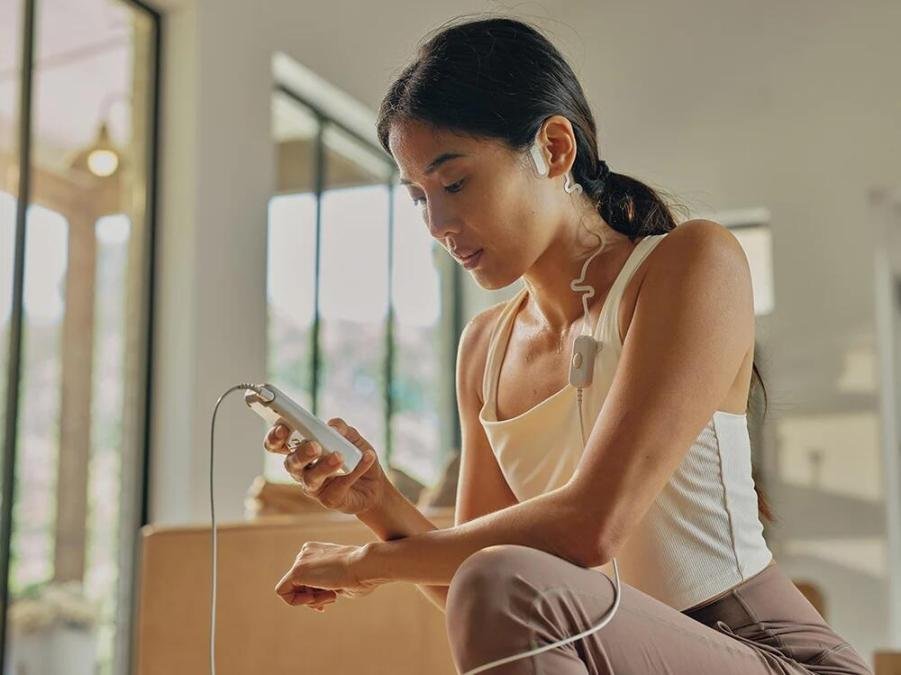 A person waring a white tank top and light brown leggings uses the OhmBody.
